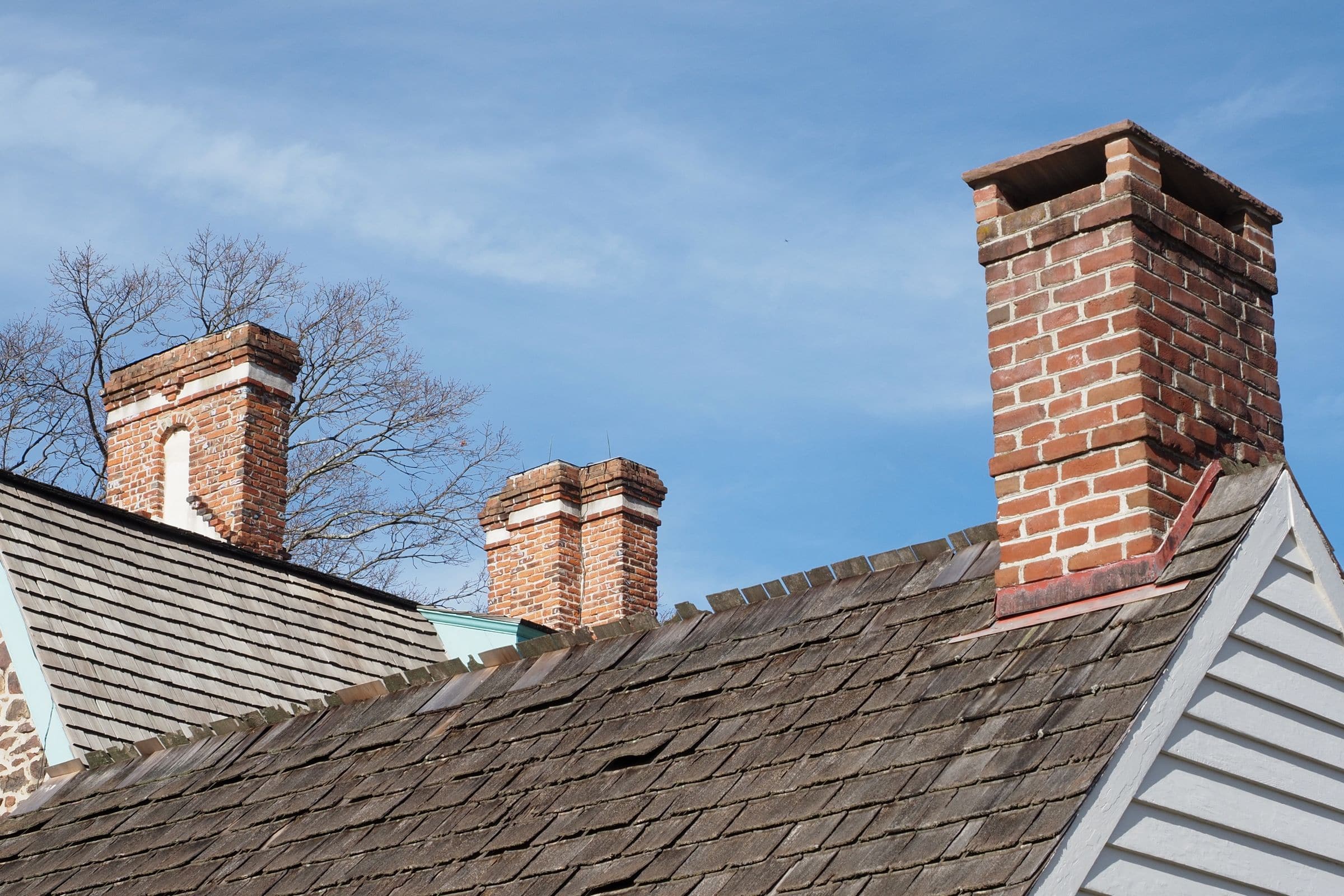 Red brick chimneys rising from a shingled roof against a blue sky